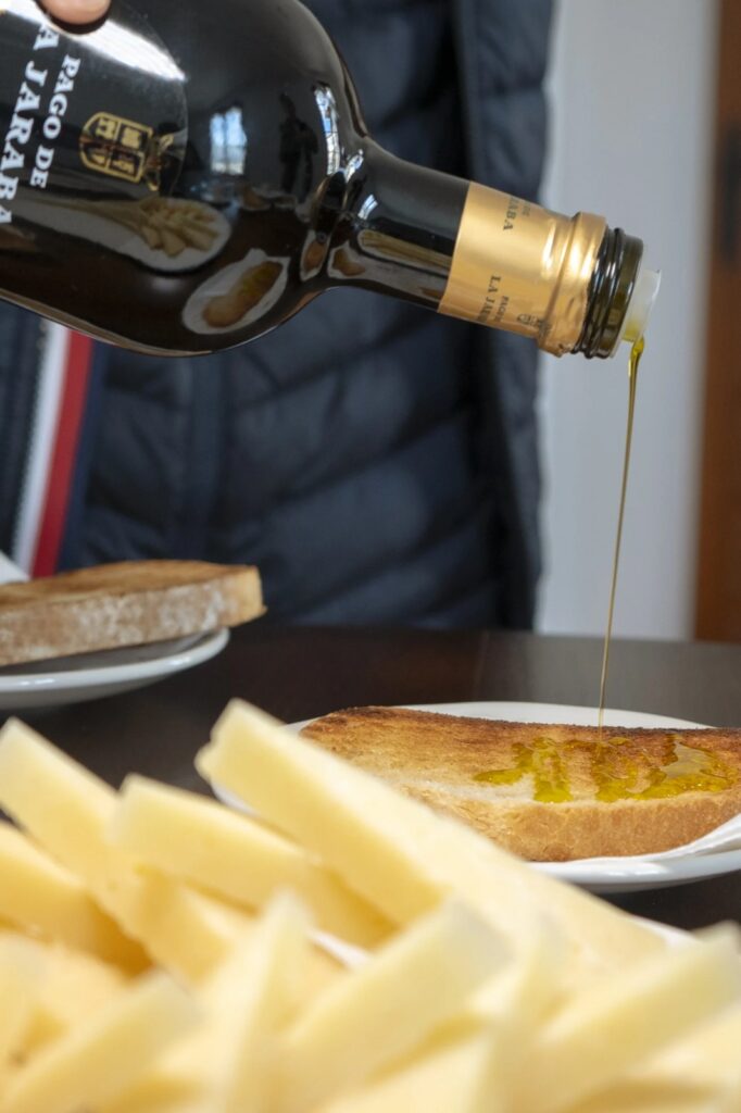 Aceite de oliva virgen extra cayendo sobre una tostada junto a queso manchego, en una experiencia gastronómica de la que podrás disfrutar en la casa rural La Moravieta.